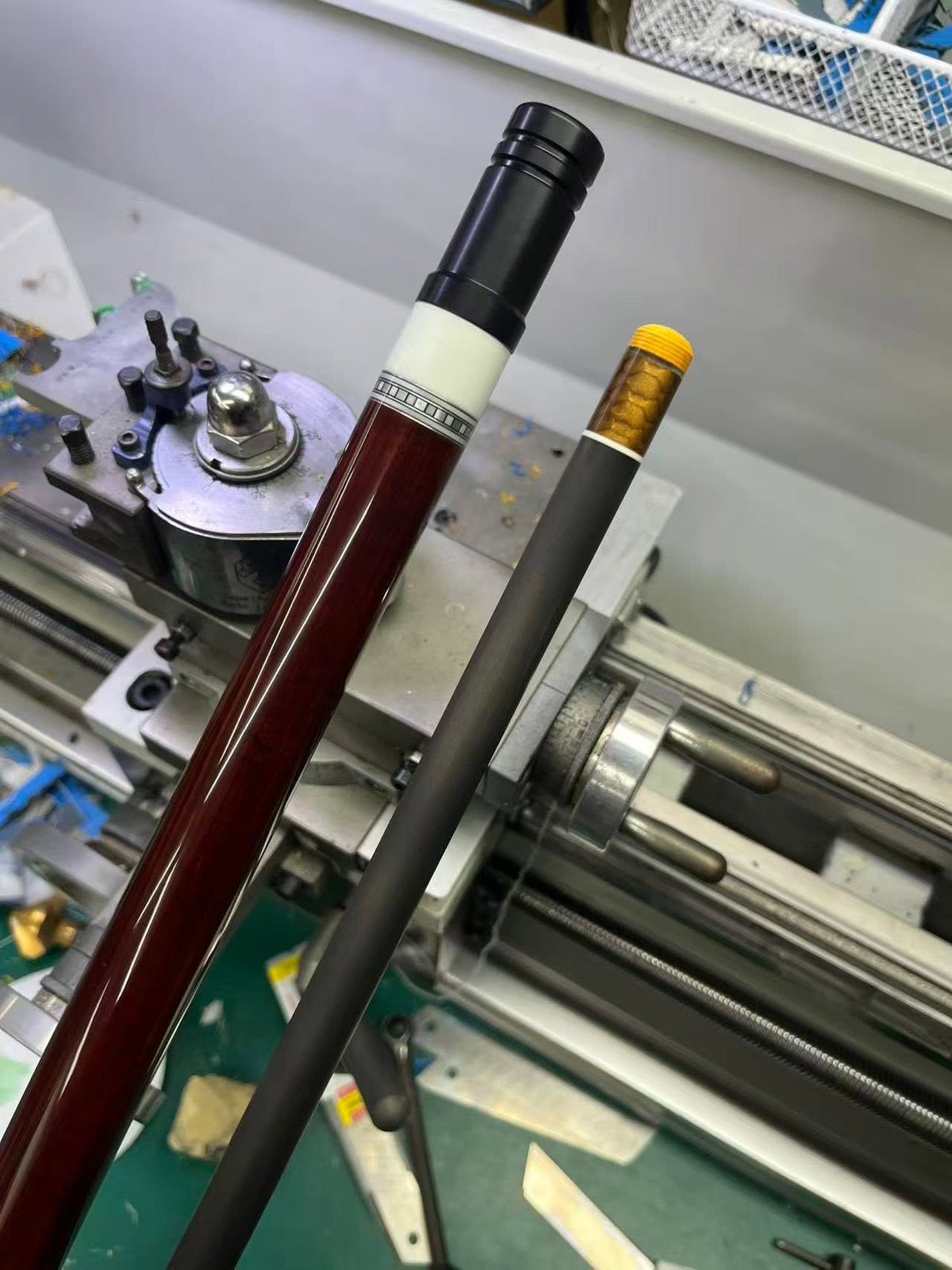 Deep red gloss cue butt beside a carbon fibre shaft with a gold inlay ring