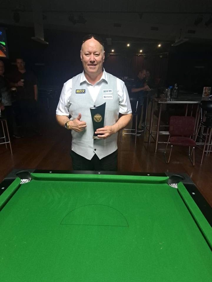 Pool player standing behind a pool table holding a tournament trophy