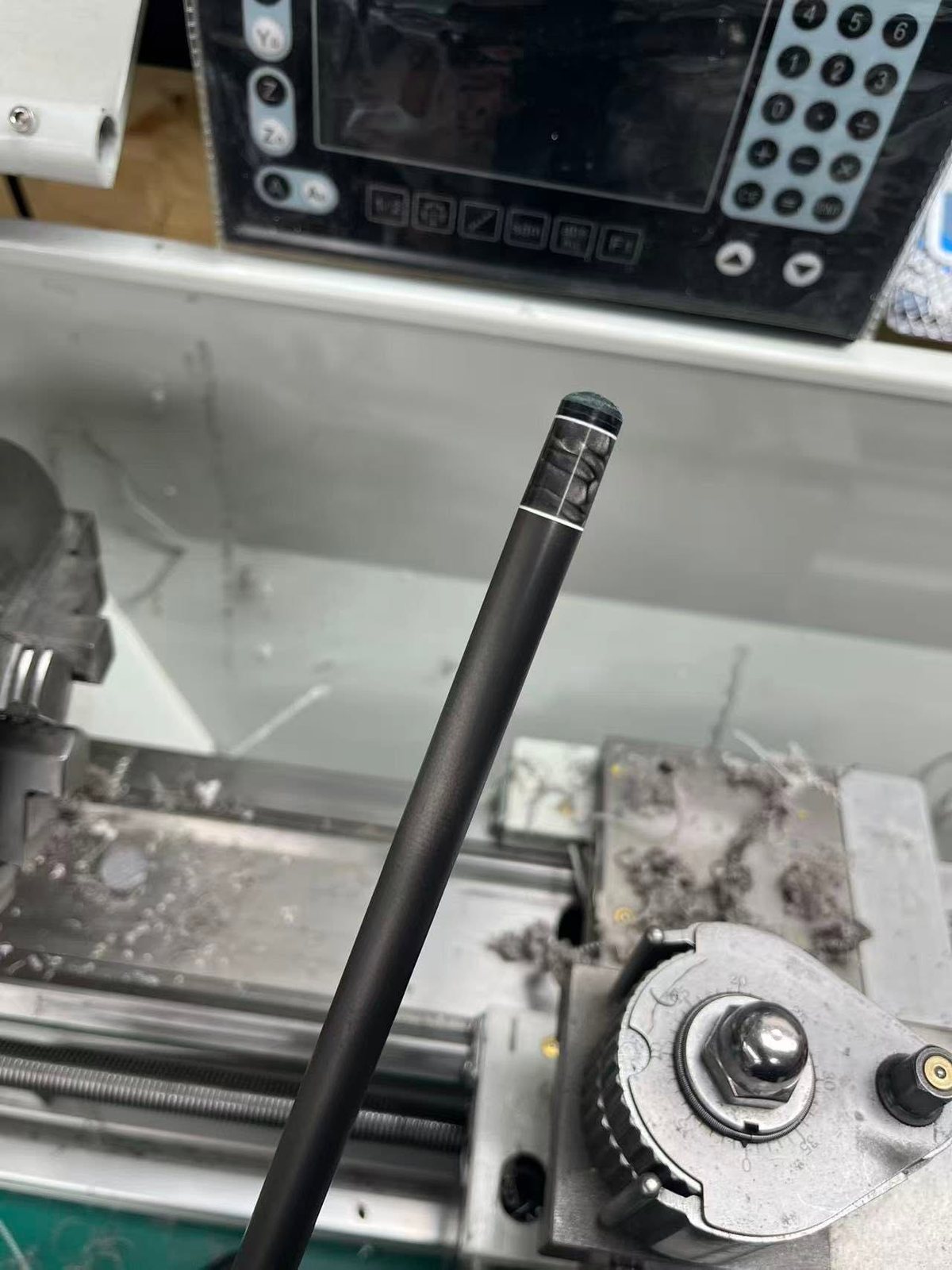 Close up of a carbon fibre shaft tip with a black pearl inlay ring on the lathe