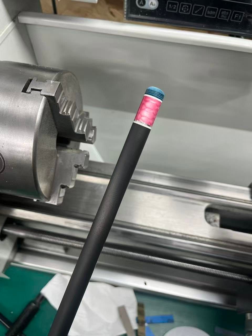 Carbon fibre shaft with a pink inlay ring and blue tip being finished on the lathe