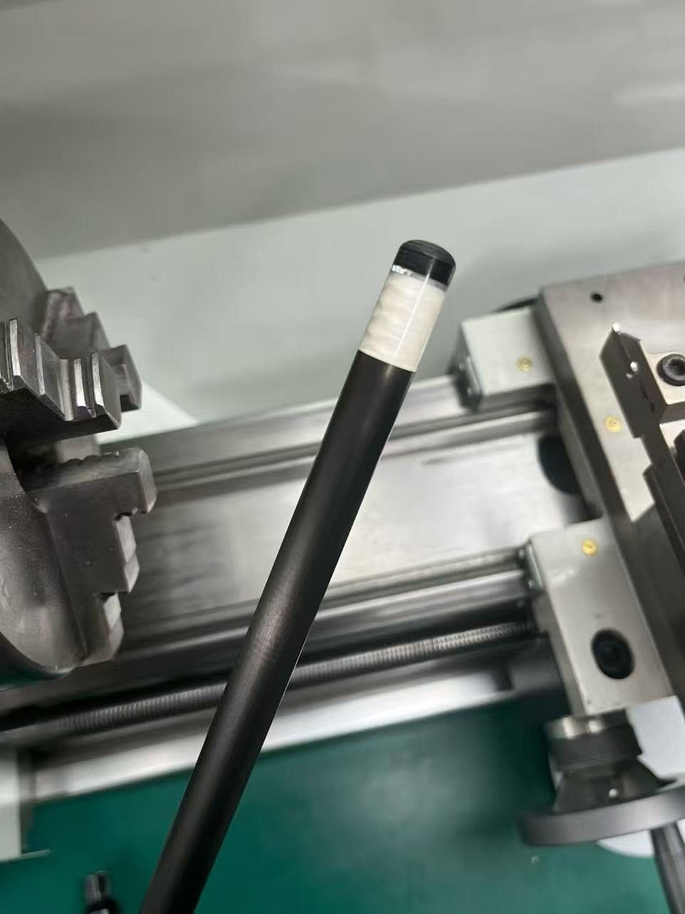 Carbon fibre shaft with a white inlay ring being finished on the lathe