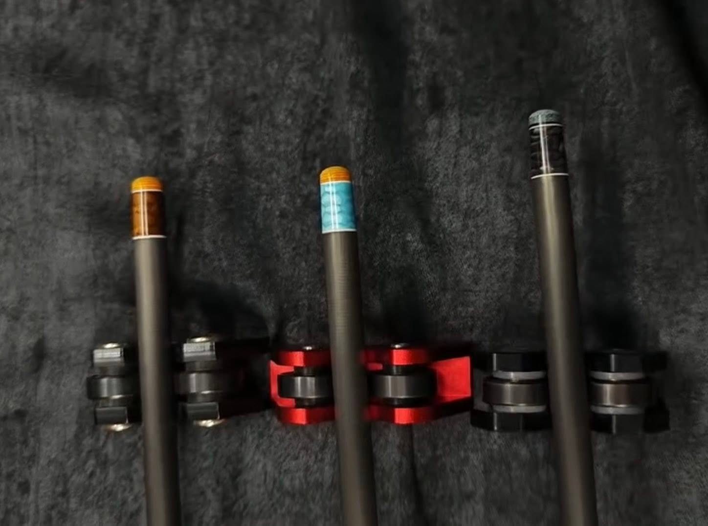 Three Remarkable Cues carbon fibre shafts with custom coloured inlay rings resting in a cue stand
