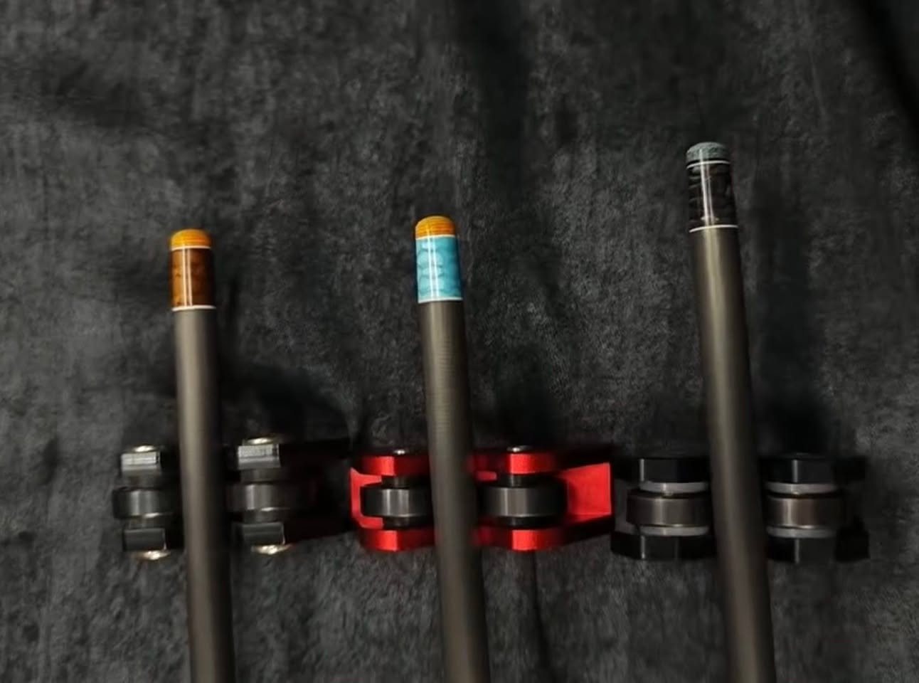 Three carbon fibre shafts with different coloured inlay rings held in a cue stand